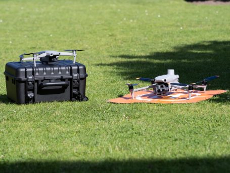 Zwei Drohnen auf einer grünen Wiese, eine in der Mitte, eine daneben in Koffer.