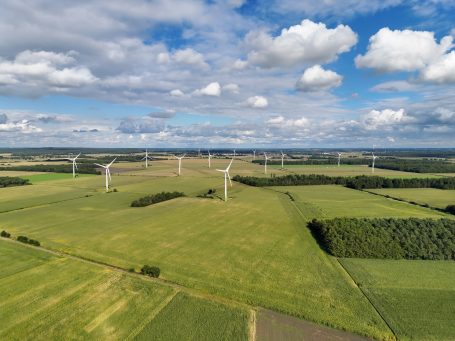 Landschaft mit Windkraftanlagen und einem weiten, grünen Feld unter einem wolkigen Himmel.